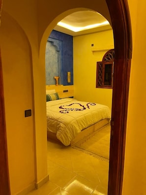 Un couloir étroit mène à une chambre à coucher qui contient un lit, un mur d’accent bleu et un cadre de porte en bois.