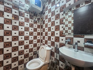 A bathroom with a patterned tile wall, a toilet, and a sink with a mirror above it. - Oly Hotel Shiva Inn (New Delhi)