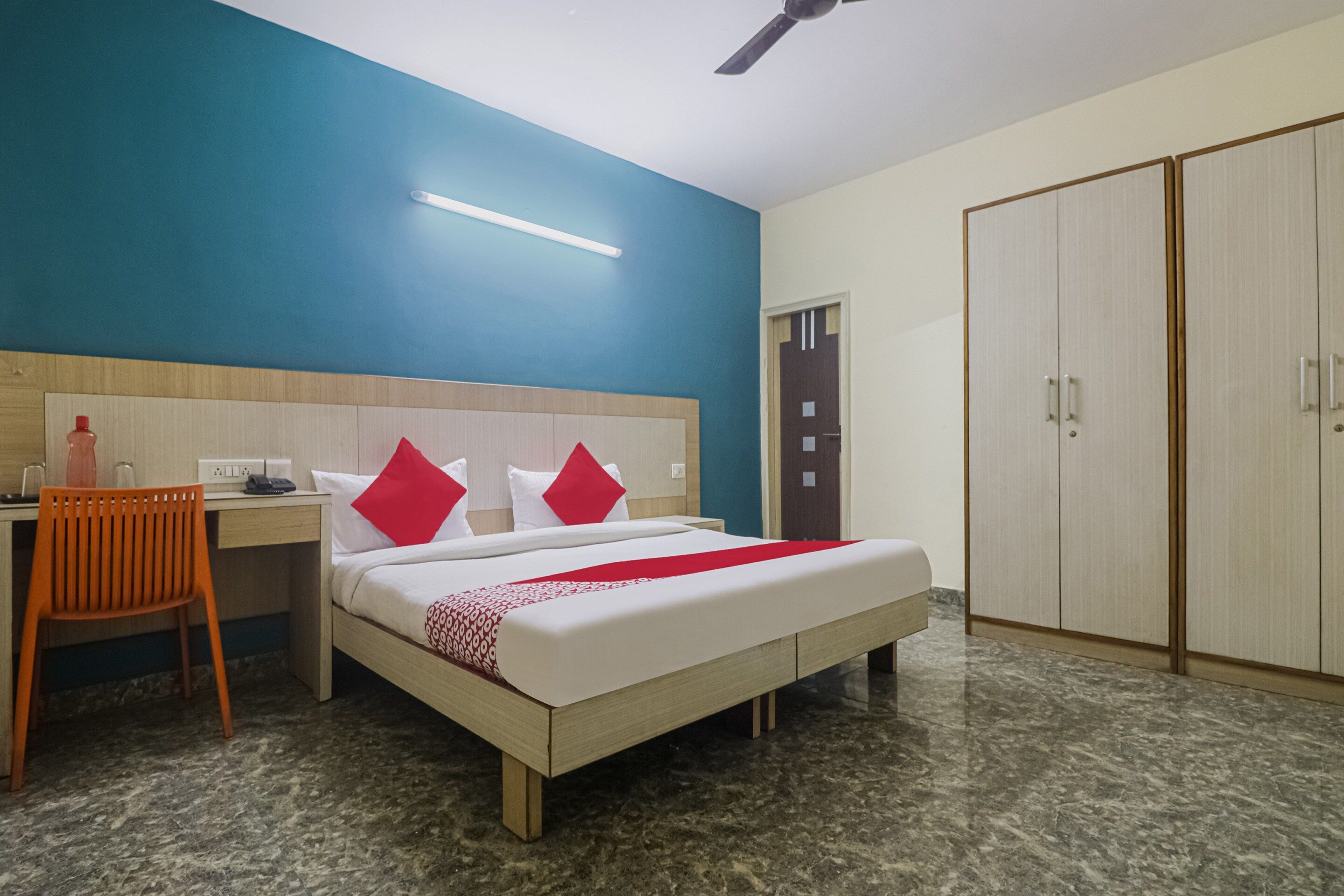 A hotel room with a bed, a desk, a chair, a wardrobe, and a ceiling fan.