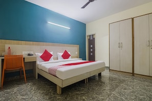 Ein Hotelzimmer mit Bett, Schreibtisch, Stuhl, Kleiderschrank und Deckenventilator.