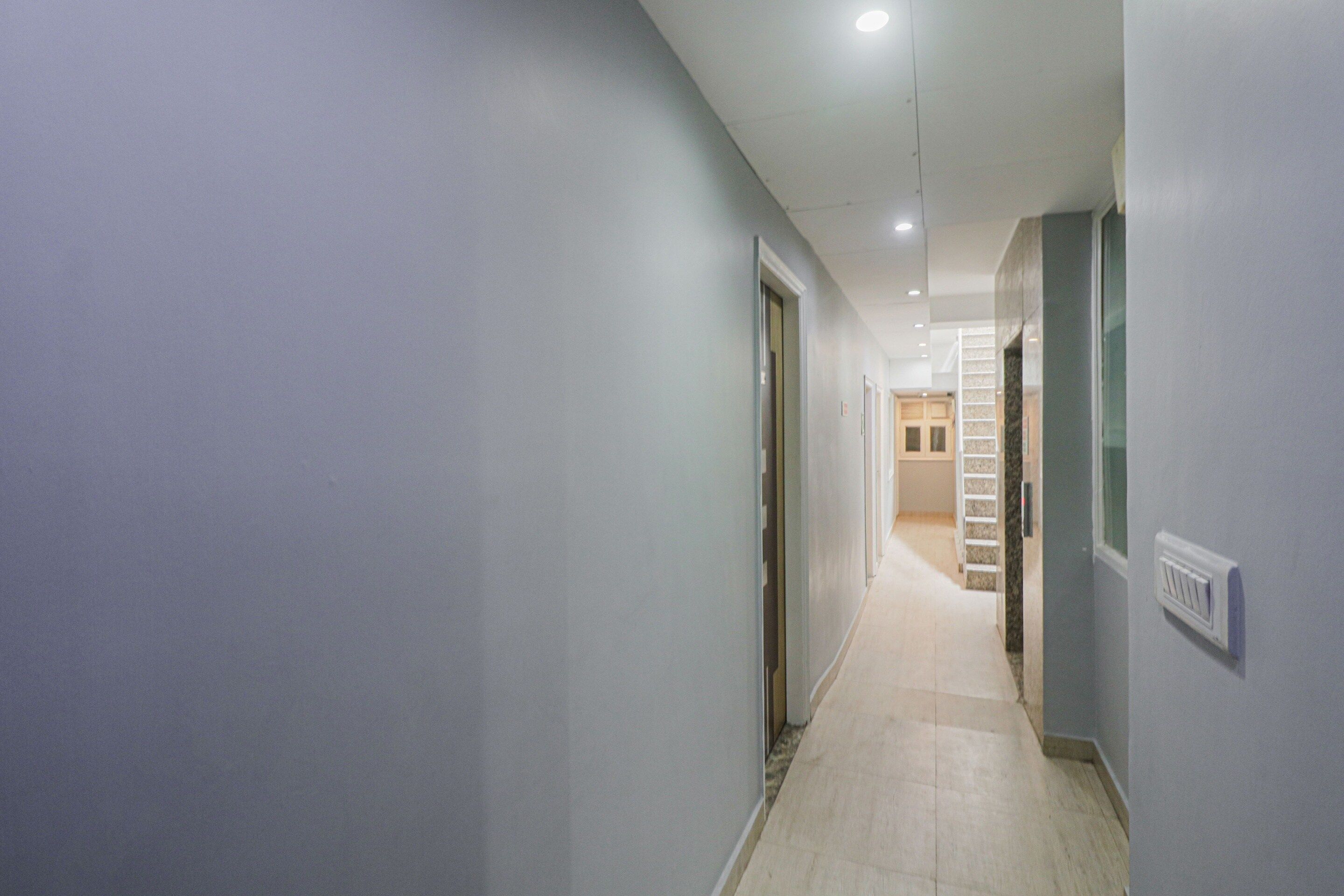 A narrow hallway with a light-colored floor, white walls, and a door at the end leading to a staircase.