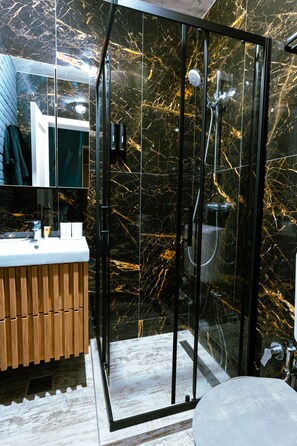 A modern bathroom with a glass shower enclosure, a wooden vanity, and a marble backsplash.