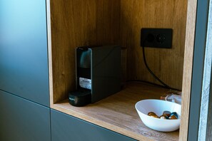 A small wooden cabinet with a black coffee maker and a bowl of coffee pods.