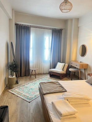 A bedroom with a bed, a desk, a chair, a potted plant, and a window with curtains. - Marsel Rooms (İzmir)