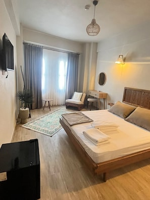 A modern hotel room with a large bed, a desk, a chair, and a window with curtains. - Marsel Rooms (İzmir)