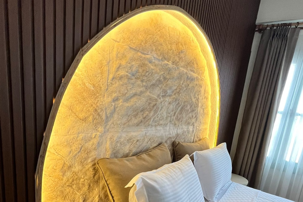 A bed with white bedding, a wooden nightstand, and a curved headboard with a textured design.