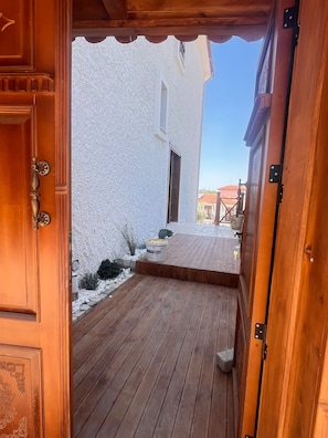 A wooden door leading to a covered wooden deck with a white building in the background. - Marsel Rooms (İzmir)