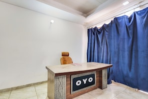 Un comptoir d’accueil avec une enseigne indiquant « OYO », dans une pièce aux murs blancs, avec un rideau bleu et un sol carrelé.