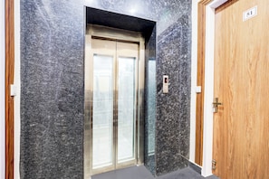 A modern elevator with a metallic finish, a wooden door to the right, and a marble wall. - Hotel O by OYO ETERNAL RESIDENCY (Gurugram)
