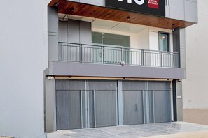 A modern building with a closed metal shutter door, a balcony with a metal railing, and a sign above the door. - Hotel O by OYO ETERNAL RESIDENCY (Gurugram)