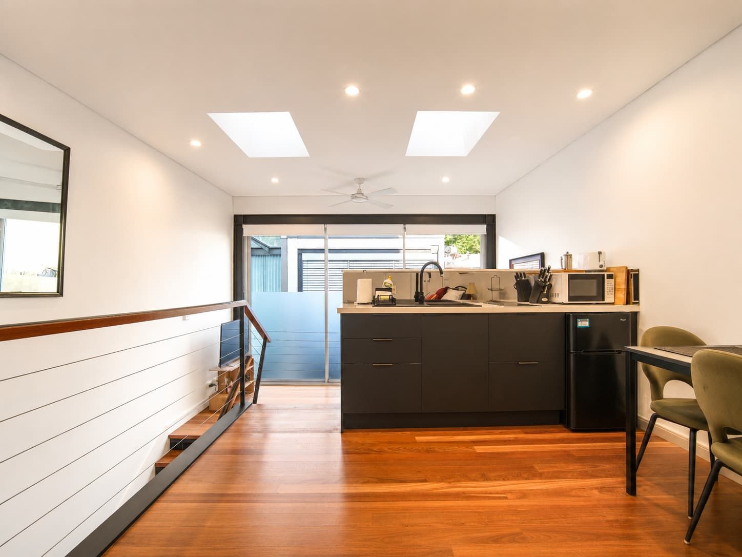 A modern kitchen with a central island, a dining area with a green chair, and a view of the outside.