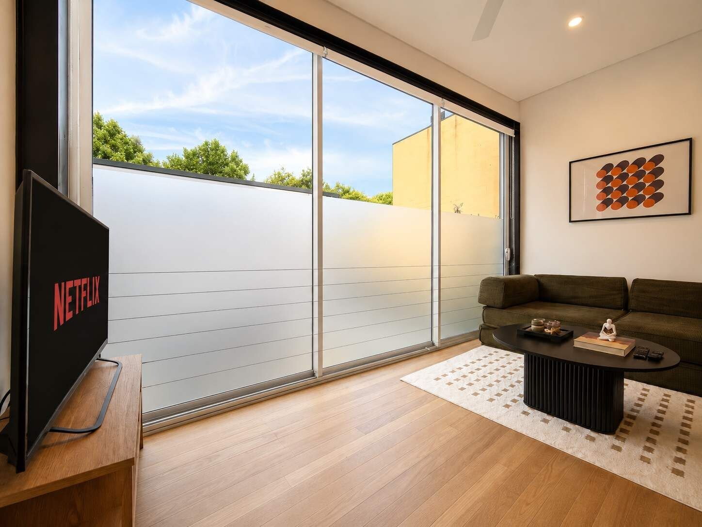 A modern living room with a sliding glass door leading to a balcony, a flat-screen TV, a sofa, and a coffee table.
