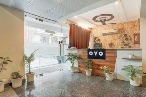 A reception area with a wooden reception desk, potted plants, and a sign that reads 'OYO'. - Hotel O Urban Sky (Gurugram)