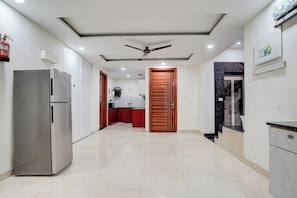 A corridor with a ceiling fan, a refrigerator, and a kitchen area with cabinets and a countertop. - Hotel O Urban Sky (Gurugram)