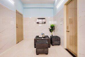 Una camera d'albergo con pavimento in marmo, un tavolino con una teiera, una pianta in vaso e due pouf.