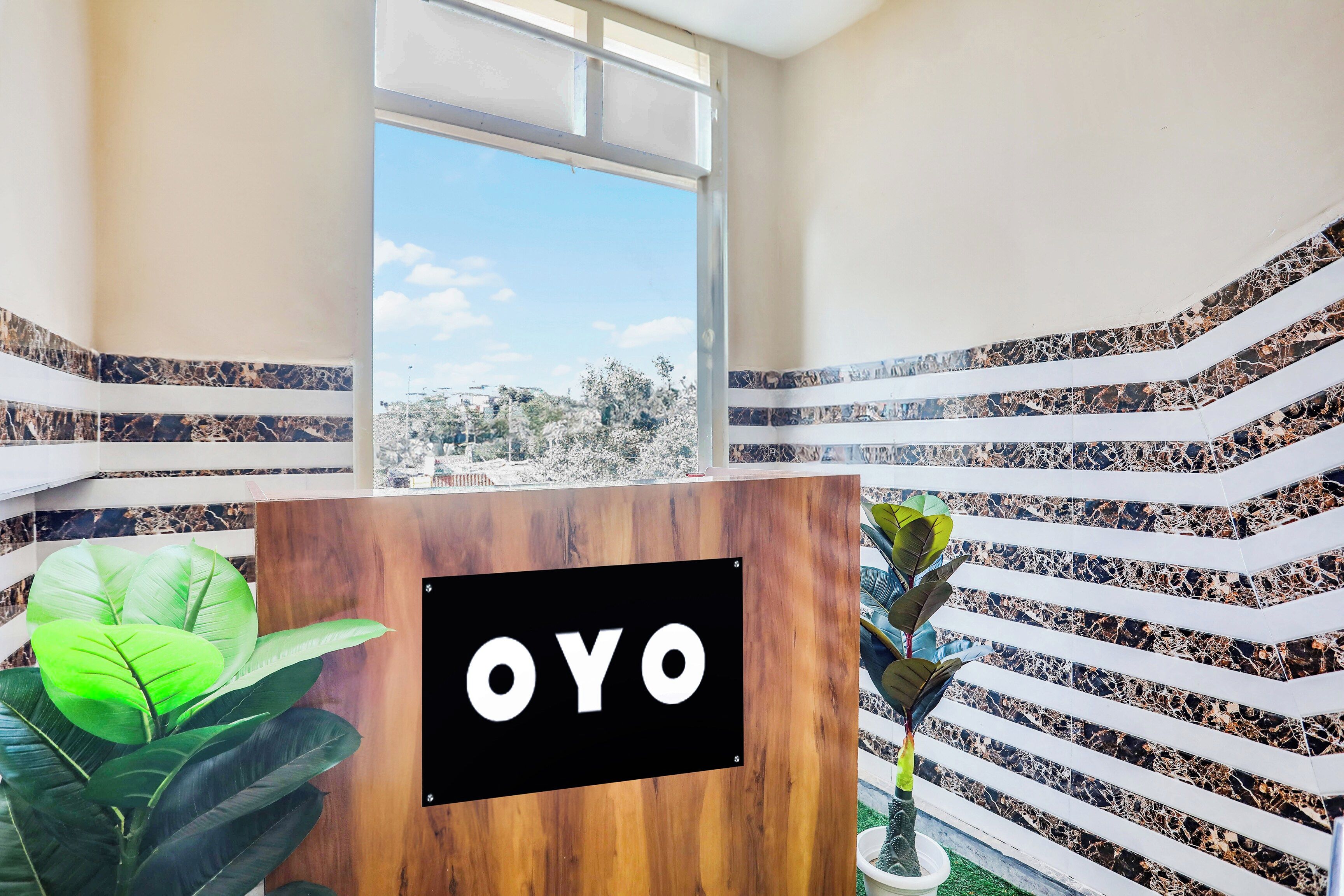 A reception desk with a sign reading 'OYO' in a hotel lobby with a view of a cityscape through a large window.