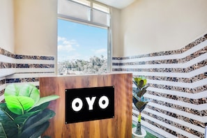 Una reception con un cartello che recita 'OYO' nella hall di un hotel, con vista sulla città attraverso un'ampia finestra.