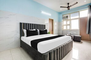 A modern bedroom with a bed, a ceiling fan, a window, and a small table with a plant. - Hotel O Safe & Sure Residency (Gurugram)