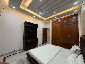 A bedroom with a bed, wardrobe, and a television. - Road B (New Delhi)