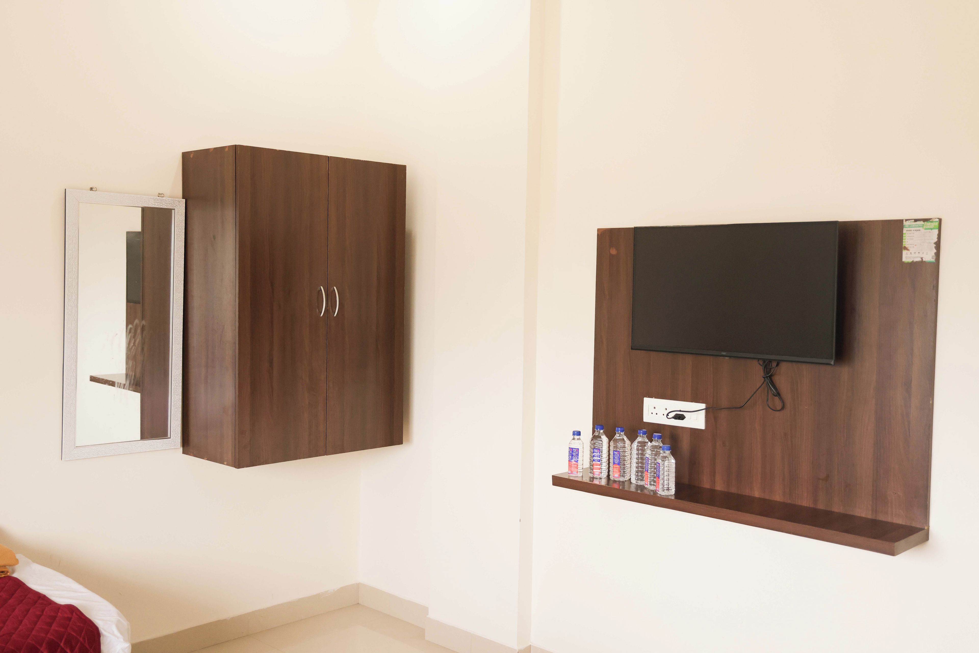 Una habitación con armario, espejo, televisor montado en la pared y estante con agua embotellada.