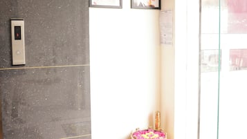 Un área de recepción con pared de mármol, un indicador digital de ascensor y una pequeña mesa con un cuenco decorativo.