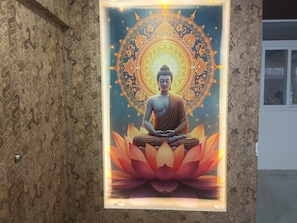 A framed artwork of a seated figure on a lotus base, surrounded by ornate patterns. - RITHANYA SUITES (Bengaluru)