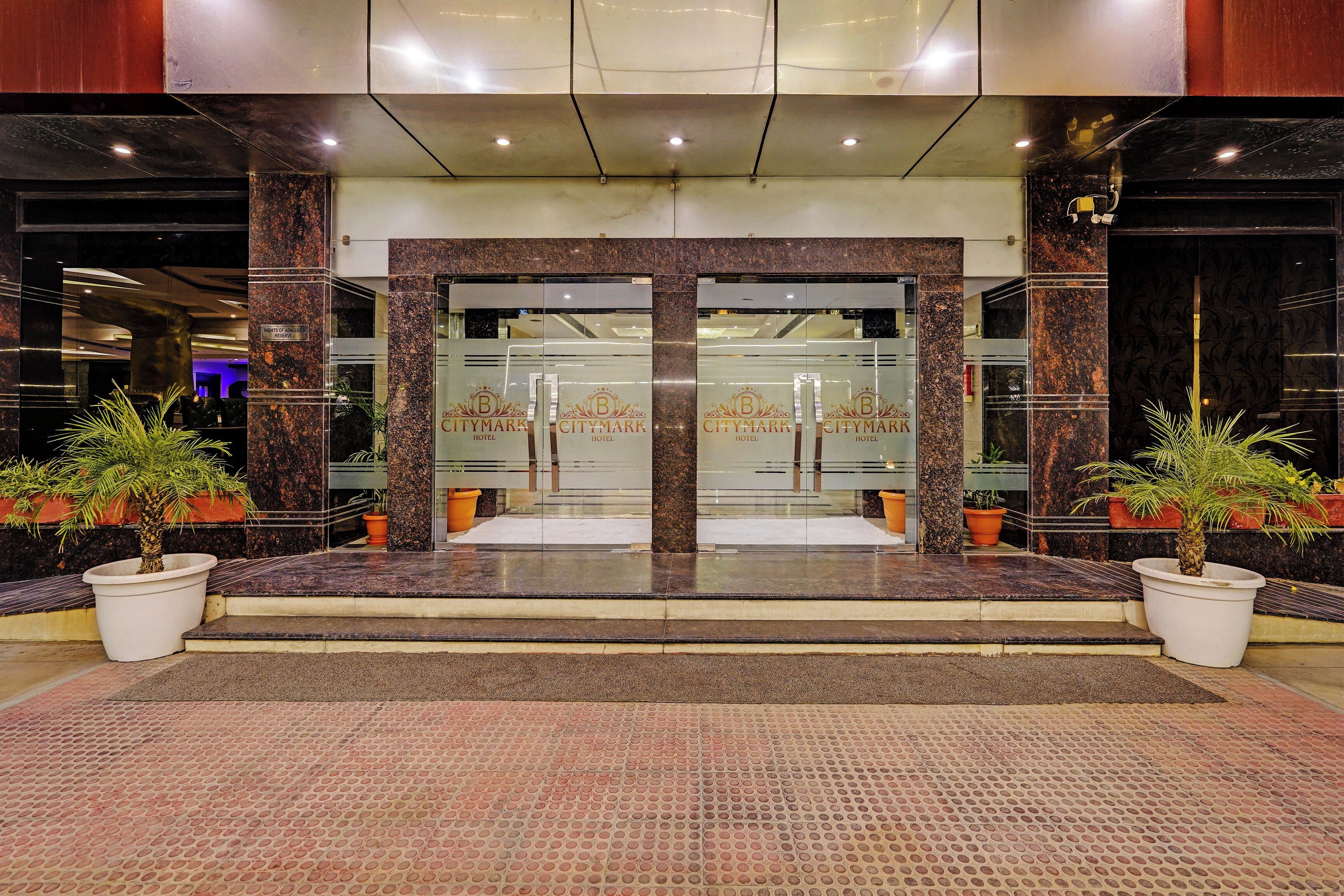 A hotel entrance with a glass door, potted plants, and a tiled floor.