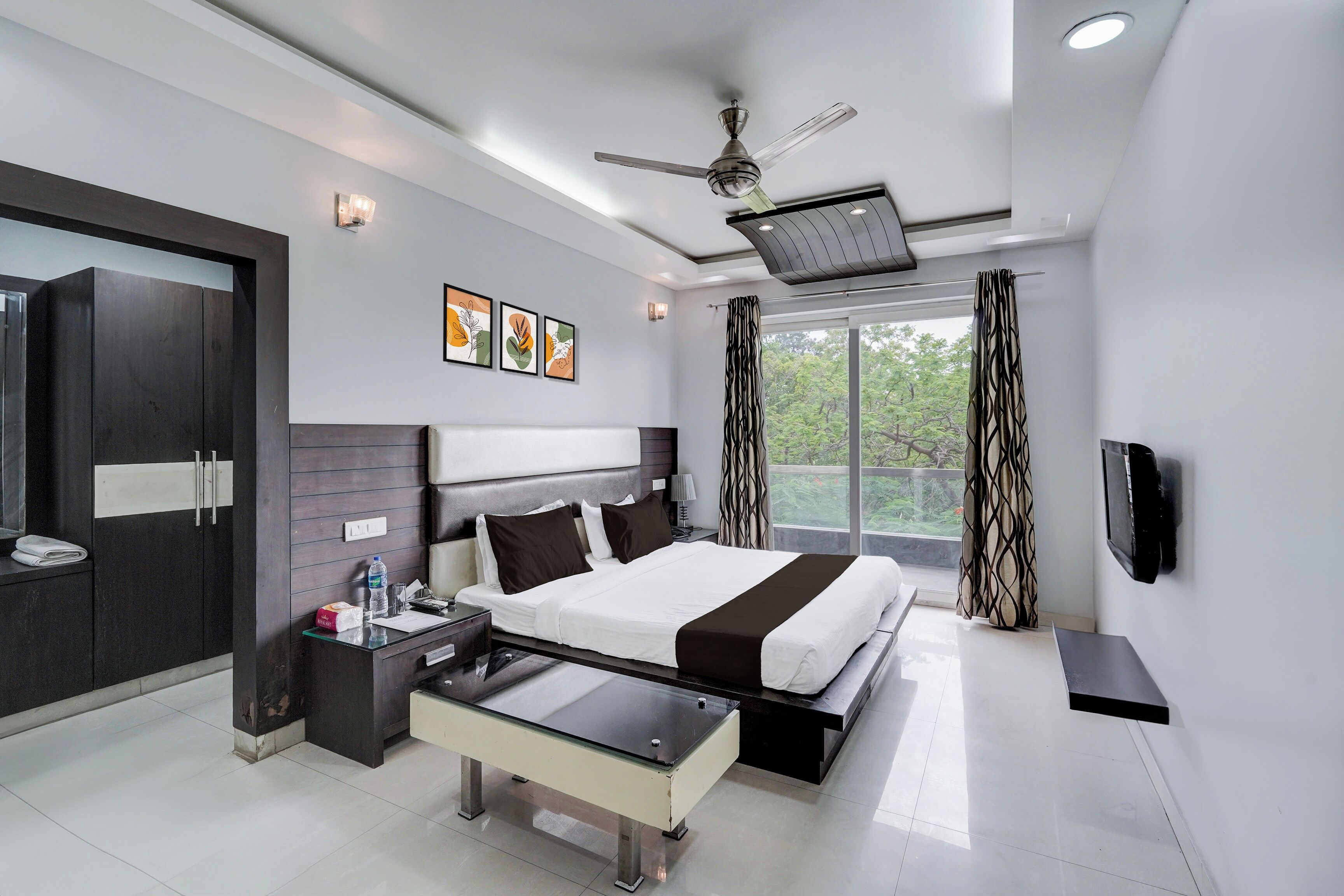 A modern hotel room with a large bed, a desk, a wardrobe, and a ceiling fan.