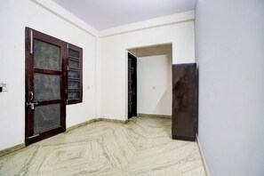 Una habitación con pared blanca, puerta de madera con mosquitera, suelo estampado con diseño de mármol y un mueble oscuro.