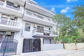 Un edificio residencial de varios pisos con balcones, unidades de aire acondicionado y un acceso con portón.