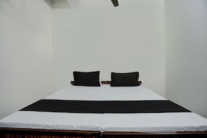 A simple, unadorned room with a single bed, two pillows, and a plain white wall. - Hotel O Swagat (Taoru)