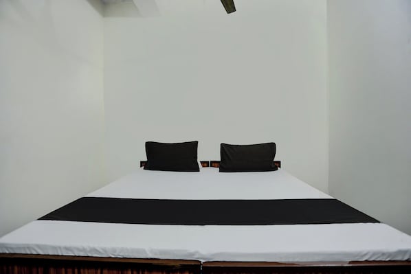 Una habitación sencilla y sin adornos, con una cama individual, dos almohadas y una pared blanca lisa.