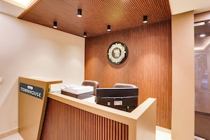 En receptionsdisk med et skilt der viser 'OYO TOWNHOUSE', en træpanelvæg og en rund skilt med 'MÁ 32'.