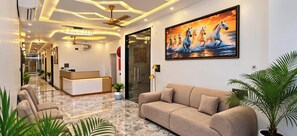 A hotel lobby with a reception desk, seating area, and a large painting of horses. - Hotel Shyamagiri (Ranopali)