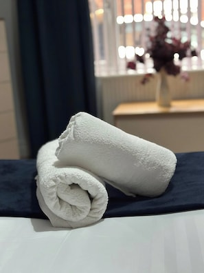 Una toalla blanca doblada con cuidado sobre una cama con cubrecama azul oscuro.