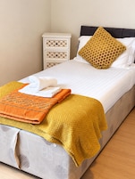 Una cama bien hecha con cubrecama blanco, manta color mostaza y almohada con estampado de panal.