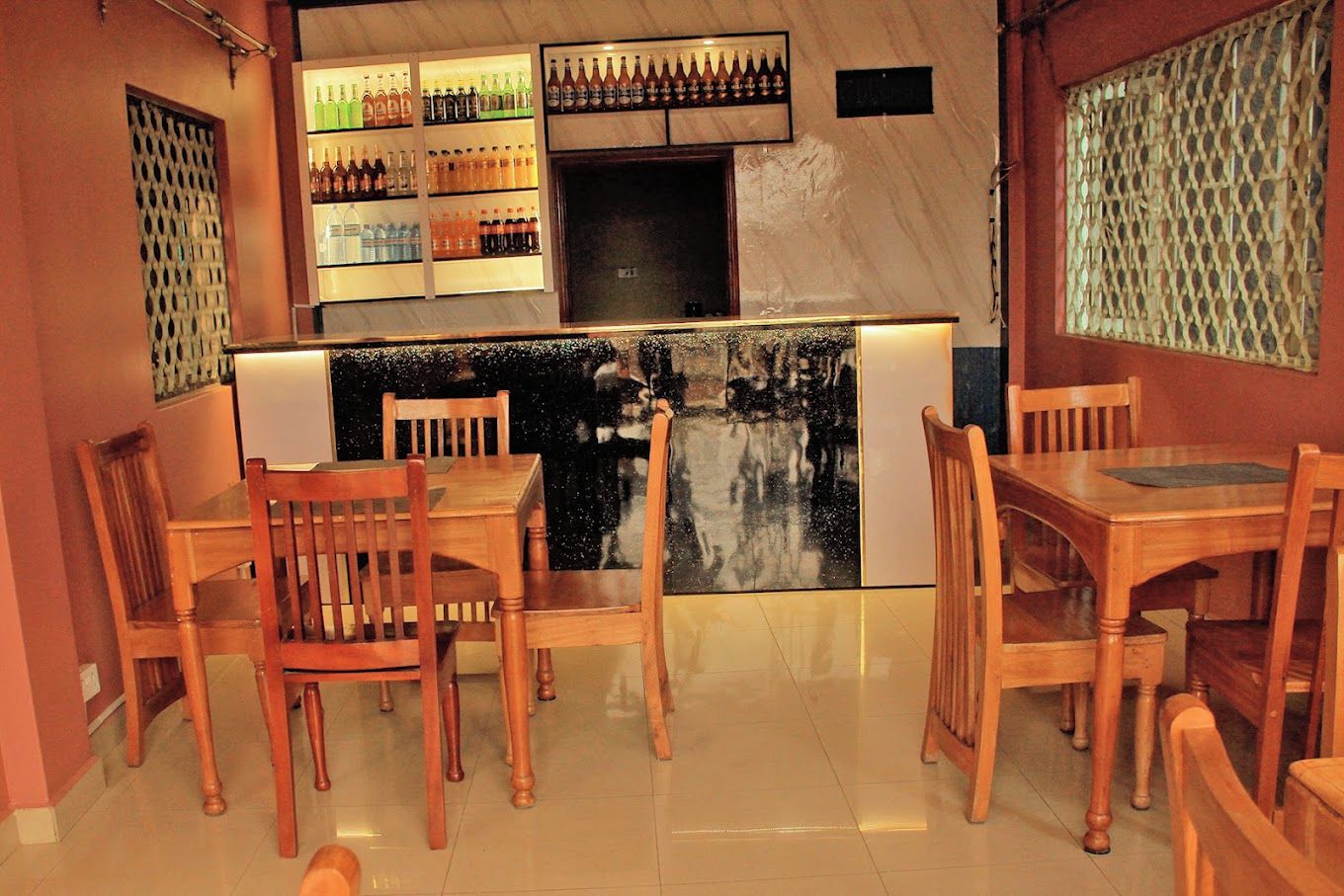 A restaurant interior with wooden tables and chairs, a bar area with bottles, and a decorative wall.