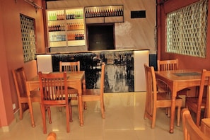 Interior de un restaurante con mesas y sillas de madera, una zona de bar con botellas y una pared decorativa.