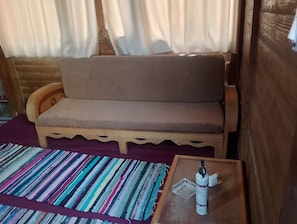 Puisesta sohvasta löytyy tyyny, lattialla on raidallinen matto ja pienen pöydän päältä löytyy pullo ja lasi.