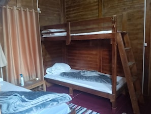 Puinen kerrossänky, jossa on tikkaat, pieni pöytä pullon kanssa ja peitto lattialla.