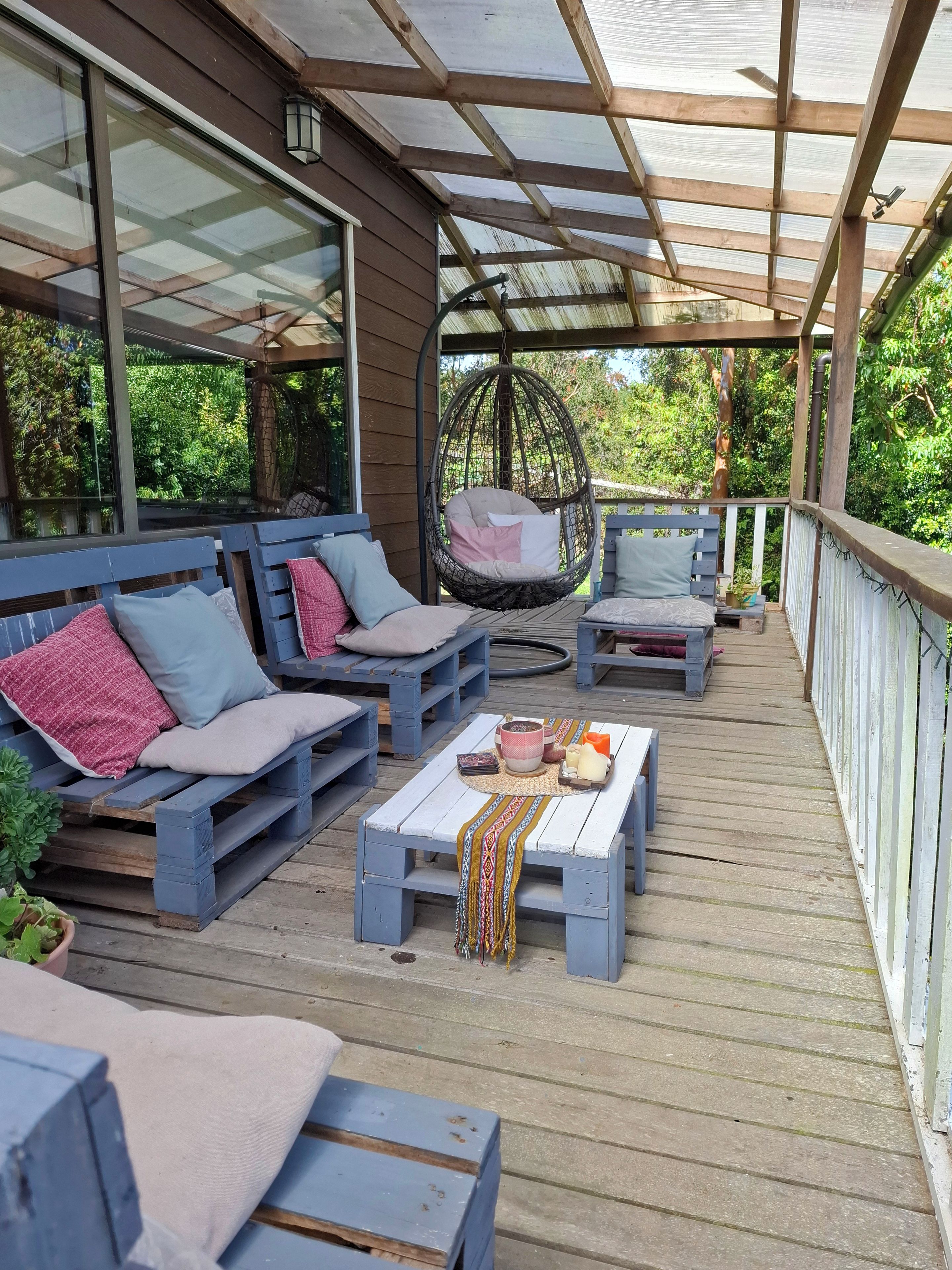 A covered outdoor seating area with wooden furniture, a hanging chair, and a table with decorative items.