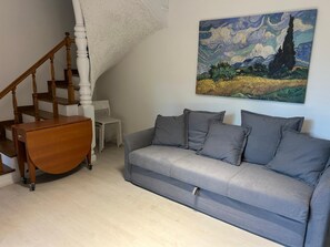 Un salon avec un canapé gris, un escalier en bois et un tableau représentant un paysage.