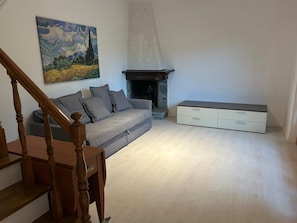 Un salon avec un canapé gris, un tableau au mur, une cheminée et un escalier.