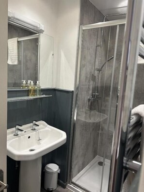 A modern bathroom with a glass-enclosed shower, a white sink, and a mirror above it. - Broadway Country House (Laugharne)