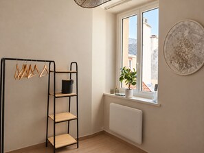 Ein Zimmer mit einem schwarzen Metallregal, einem Heizkörper, einem Fenster mit Blick auf Gebäude und einer Blumentopf auf dem Fensterbrett.