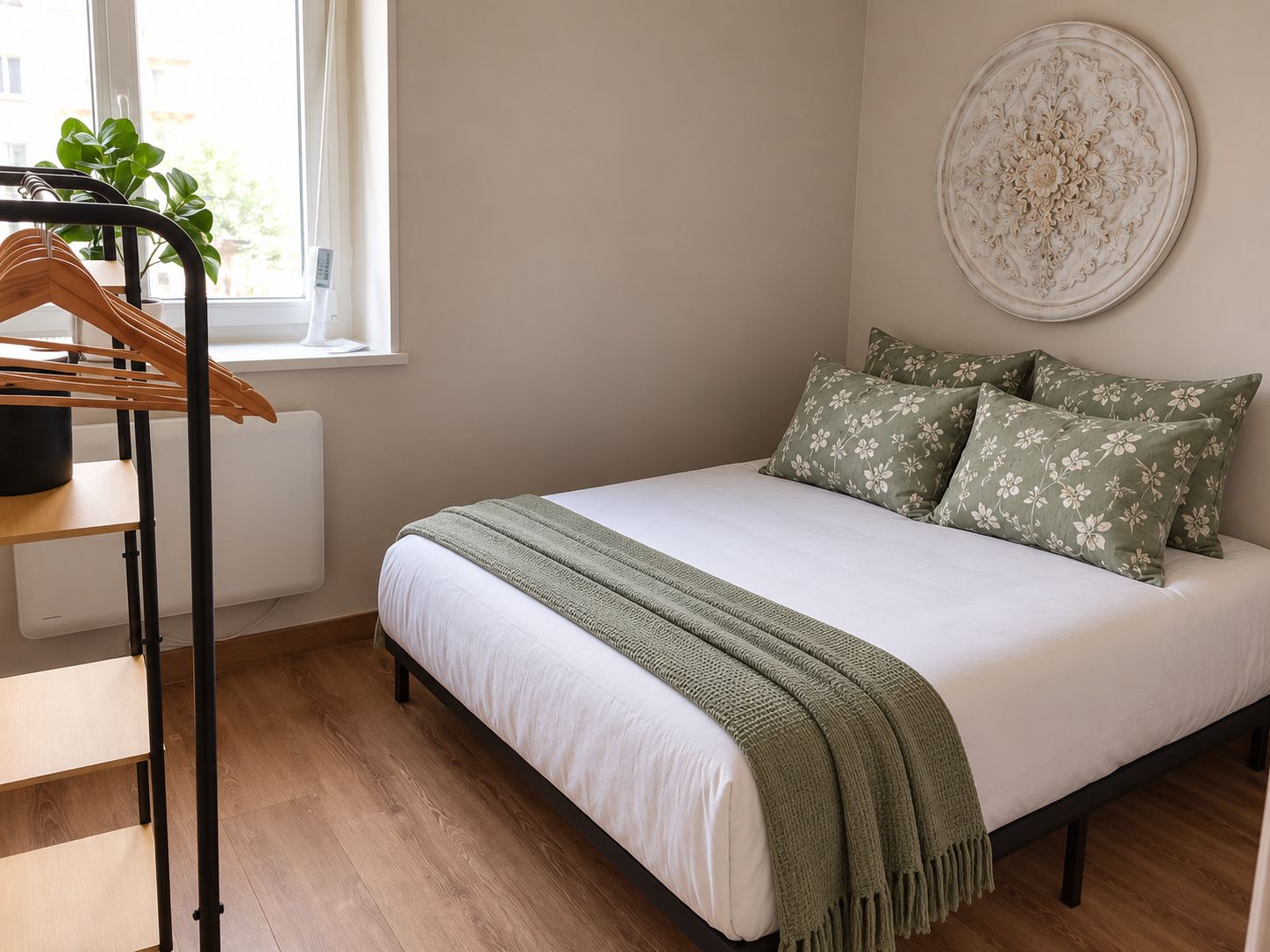 Un dormitorio con cama, radiador, ventana, planta y decoración en la pared.