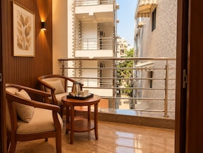 A balcony with two wooden chairs, a small table with a tray, and a framed picture on the wall. - Hotel Radhe Elite At Delhi Airport  (New Delhi)
