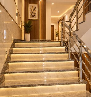A staircase with marble steps and a metal railing, leading to a wooden door. - Hotel Radhe Elite At Delhi Airport  (New Delhi)