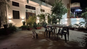 Un patio con un perro, mesas al aire libre y un edificio de varios pisos con balcones.