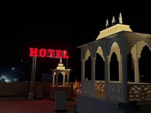 A hotel sign illuminated in red, a traditional white structure with arches, and a flag. - Hotel Aravali View (Jaipur Heritage (M Corp.) (Part))